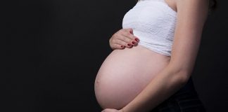 mulher grávida vista de lado com barriga de fora e com as mãos em cima e embaixo