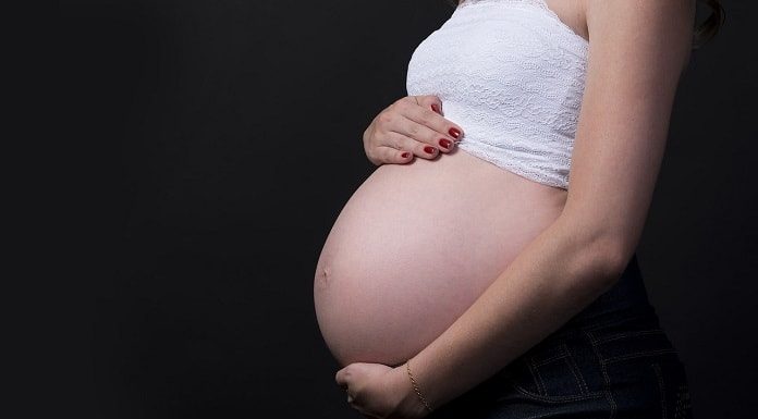 mulher grávida vista de lado com barriga de fora e com as mãos em cima e embaixo