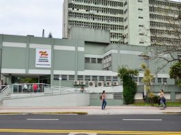 fachada do prédio do hospital vista do outro lado da rua; mulher passa na calçada