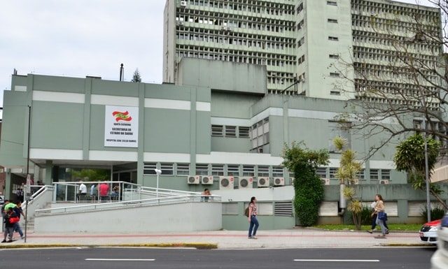 fachada do prédio do hospital vista do outro lado da rua; mulher passa na calçada