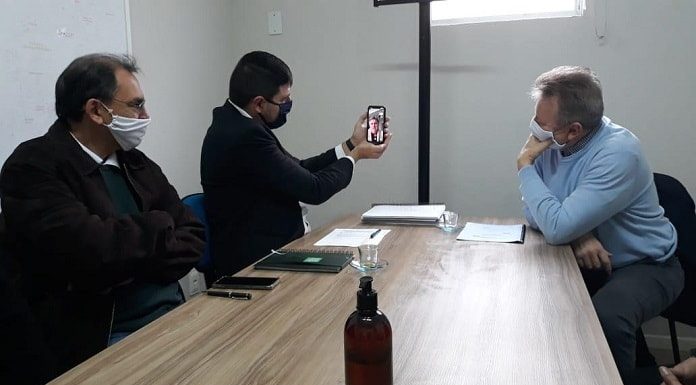 michel schlemper segura celular com transmissão de dario berger; na mesa esta maldaner e mais outro homem