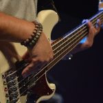 close em homem tocando contrabaixo; ele usa duas pulseiras na mão direita