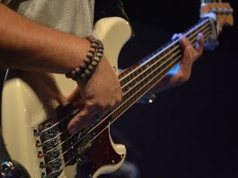 close em homem tocando contrabaixo; ele usa duas pulseiras na mão direita