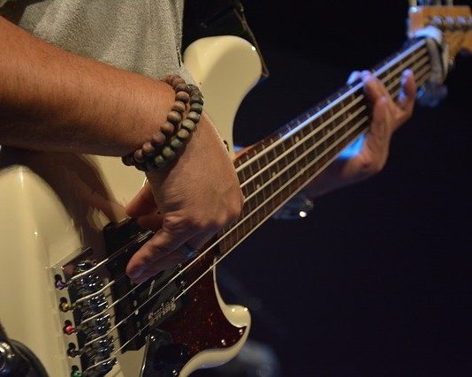 close em homem tocando contrabaixo; ele usa duas pulseiras na mão direita