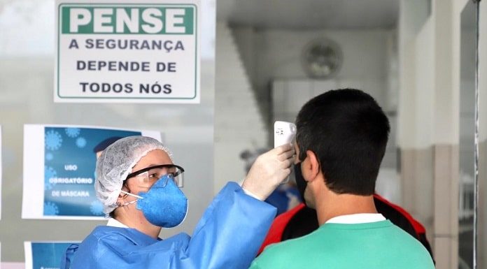 profissional de saúde completamente trajada com roupas de proteção mede a temperatura da testa de um homem