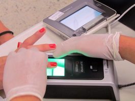 pessoa usando luvas tomas as digitais de mulher em aparelho de biometria