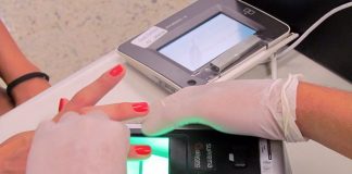 pessoa usando luvas tomas as digitais de mulher em aparelho de biometria