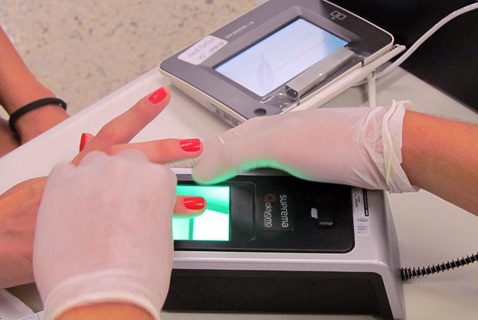 pessoa usando luvas tomas as digitais de mulher em aparelho de biometria