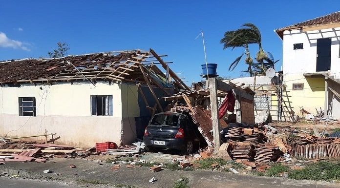 residência destelhada com carro estacionado ao lado sob muro caído e escombros em volta