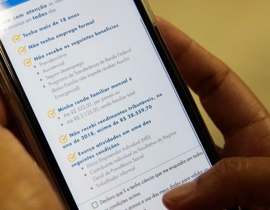 Último dia para solicitar o auxílio emergencial pessoas segurando celular em que está aberto aplicativo da caixaq