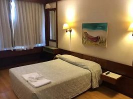 TJSC rejeita terceiro pedido do MP para limitar funcionamento de hotéis e eventos sociais cama de casal em quarto de hotel arrumado com quadro de baleeira sobre a parede, cortina fechada e luzes acesas