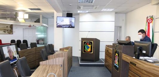 Câmara pede informações sobre transporte coletivo e requer sanitização de ambientes públicos homem usando máscara sentado, fazendo vídeo conferência