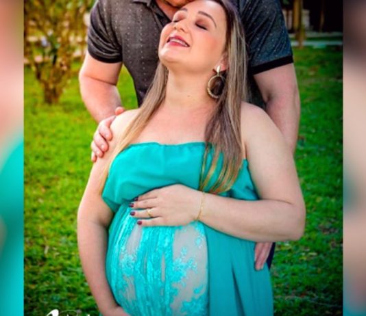 foto de book de gestante de flávia onde aparece grávida, de olhos, fechados, sorridente e sendo abraçada e beijada pelo marido