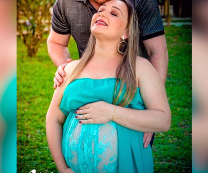 foto de book de gestante de flávia onde aparece grávida, de olhos, fechados, sorridente e sendo abraçada e beijada pelo marido