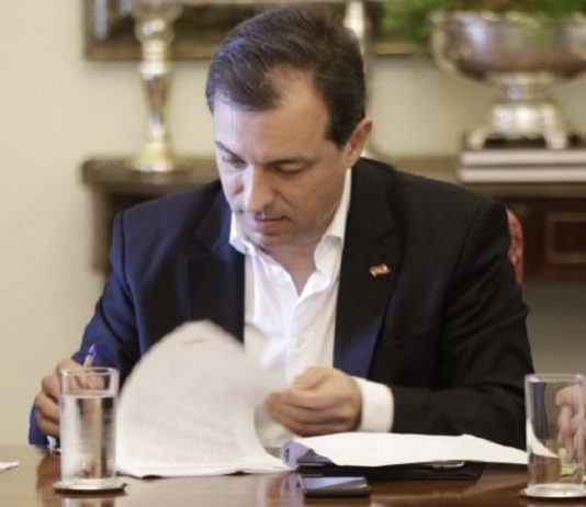 homem vestindo paletó azul, sentado assinando uns papéis