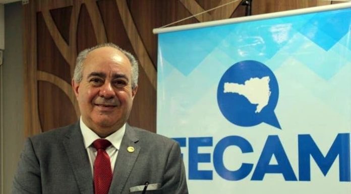 orildo sorridente para a foto ao lao de banner da fecam