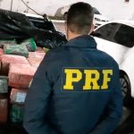 policial da prf de costas em frente à caçamba da saveiro cheia de pacotes embrulhados com plástico