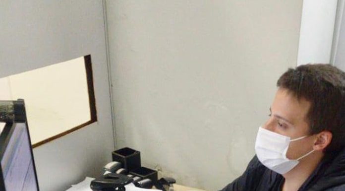 homem usando jaqueta preta e máscara banca, trabalhando em um computador