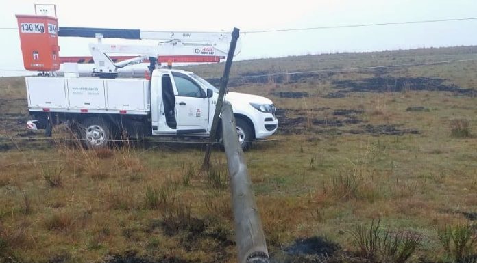 poste com a base queimada caído em área de campo queimada e caminhonete da celesc ao fundo