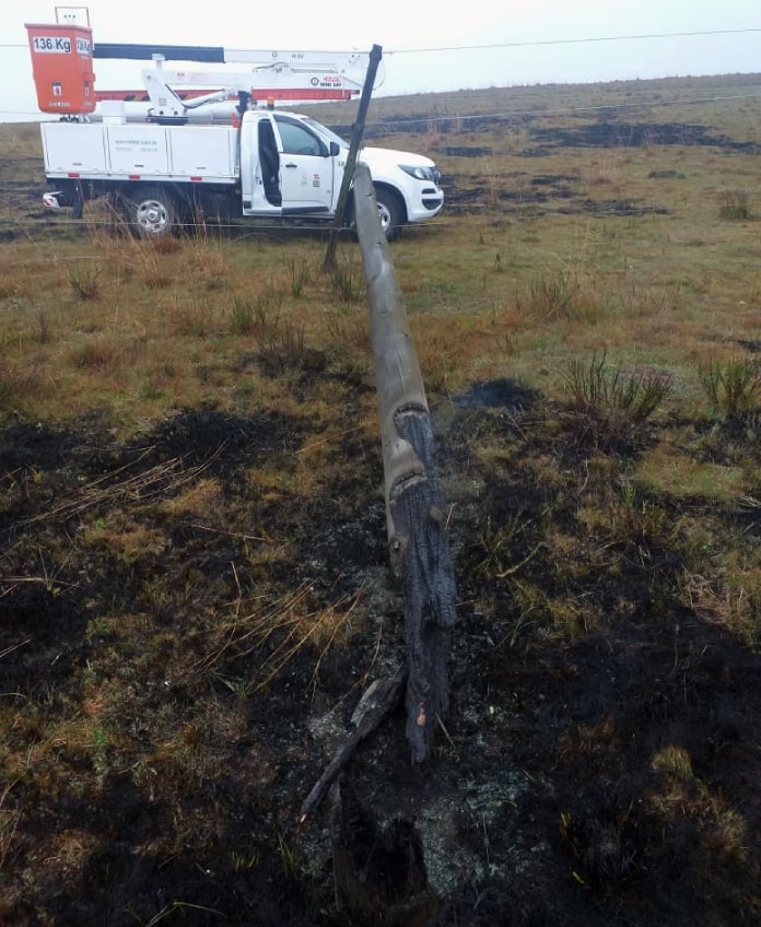 poste com a base queimada caído em área de campo queimada e caminhonete da celesc ao fundo