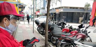 funcionária usando proteção mexe em máquina em pé na calçada com motos estacionadas na rua