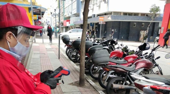 funcionária usando proteção mexe em máquina em pé na calçada com motos estacionadas na rua