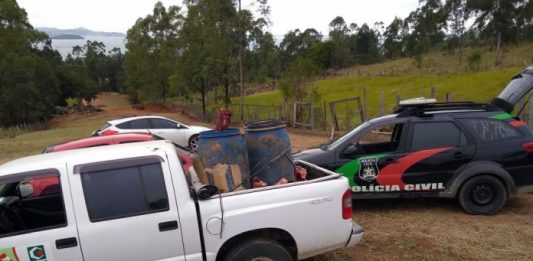 tambores com pedação de carne em caaçamba de caminhonete da cidasc; ao lado viatura da polícia civil em estrada de terra; pasto ao fundo