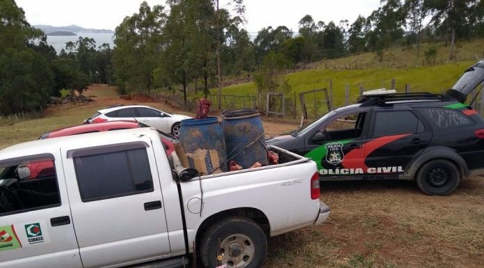 tambores com pedação de carne em caaçamba de caminhonete da cidasc; ao lado viatura da polícia civil em estrada de terra; pasto ao fundo