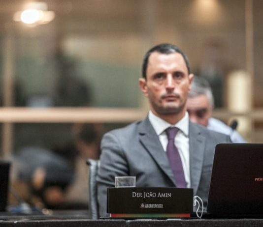 Alesc escolhe João Amin na presidência da comissão de impeachment e Vampiro na relatoria deputado joão amin na bancada da alesc olha para o alto e há uma placa com seu nome à frente junto com notebook