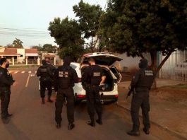 Polícia Federal deflagra operação nacional para desarticular financeiramente o PCC policias uniformizados atrás de um carro com porta malas aberto estacionado em área residencial com casas ao fundo e árvores na calçada