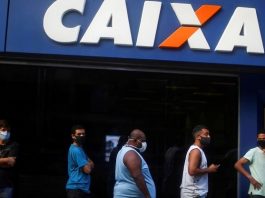 homens em fila usando mascara em frente a agencia da caixa