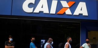 homens em fila usando mascara em frente a agencia da caixa