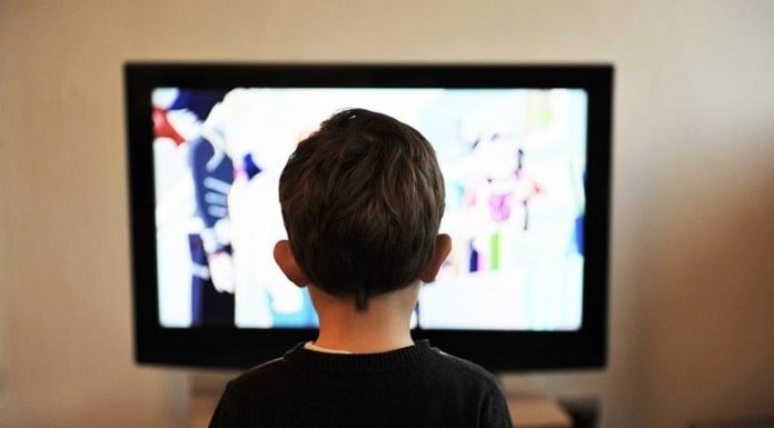 criança com camiseta preta, sentada assistindo televisão