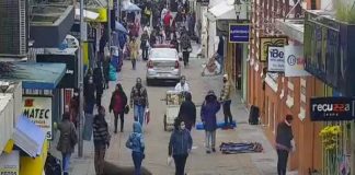 pessoas usando máscaras e roubas de frio andam no calçadão de rua no centro de florianópolis; carro da polícia; comércio em volta