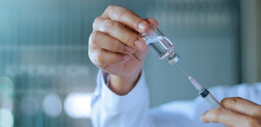 close em mãos de homem retira de ampola transparente dose com seringa