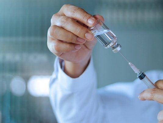 Fiocruz fecha acordo para produzir 100 milhões de vacinas de Covid-19 close em mãos de homem retira de ampola transparente dose com seringa