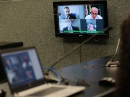 notebook em cima de uma bancada e tela ao fundo com transmissão dos deputados