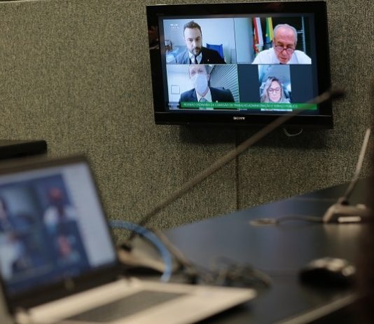 notebook em cima de uma bancada e tela ao fundo com transmissão dos deputados