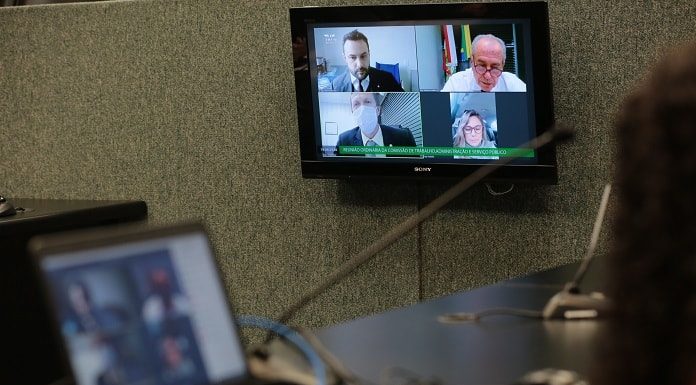 notebook em cima de uma bancada e tela ao fundo com transmissão dos deputados