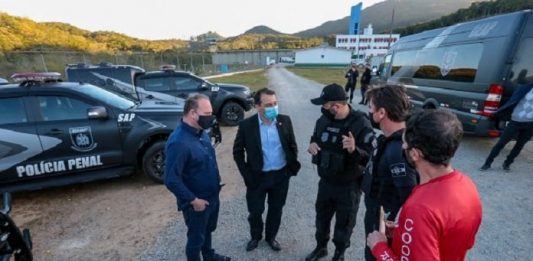 5 homens conversando de pé em frente viaturas da polícia