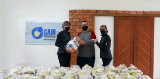 homem e duas mulheres usando máscaras posam para foto atrás de dezenas de pacotes de cestas básicas