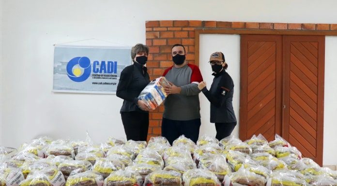 homem e duas mulheres usando máscaras posam para foto atrás de dezenas de pacotes de cestas básicas