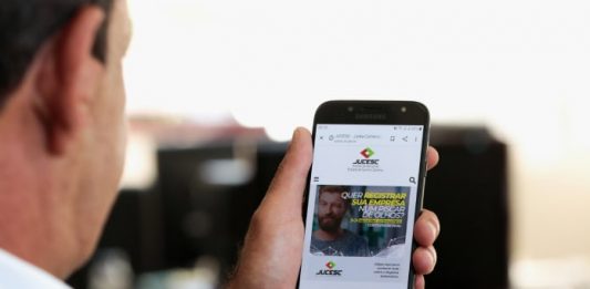 homem olha para tela de celular com site da jucesc aberto
