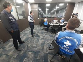 Justiça entende que estado não pode “terceirizar” completamente gestão da pandemia aos municípios motta e moisés em pé conversando com servidoras com coletes do governo estadual em diferentes mesas em uma sala acarpetada; todos usam máscaras