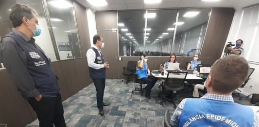 Justiça entende que estado não pode “terceirizar” completamente gestão da pandemia aos municípios motta e moisés em pé conversando com servidoras com coletes do governo estadual em diferentes mesas em uma sala acarpetada; todos usam máscaras