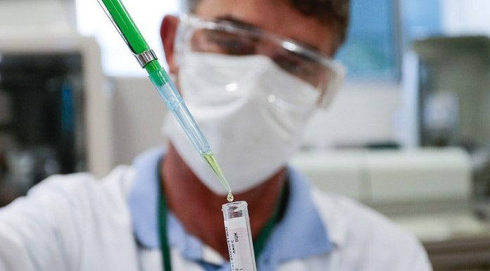 Pesquisa Tríplice Viral: homem coloca amostra de líquido dentro de ampola; ele usa máscara e óculos de proteção