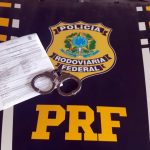 papel e algema sobre capô de viatura com distintivo e sigla da prf