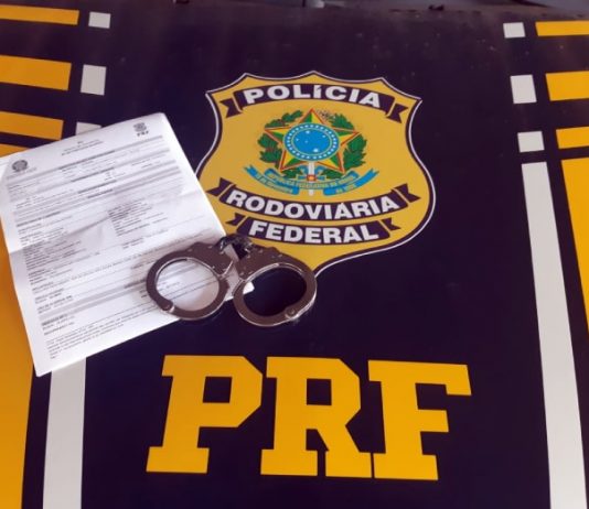 papel e algema sobre capô de viatura com distintivo e sigla da prf