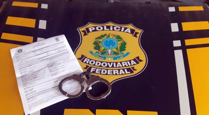 papel e algema sobre capô de viatura com distintivo e sigla da prf