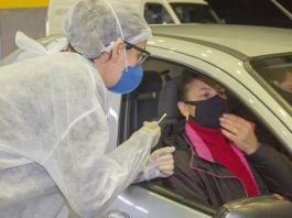 Santa Catarina registra 12.038 casos ativos de coronavírus profissional de saúde trajada com epi se inclina para janela de carro onde está mulher e homem com máscaras dentro do veículo